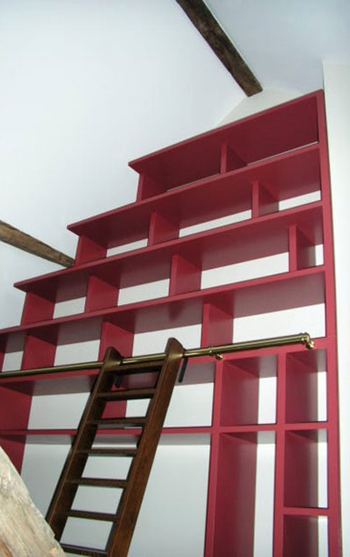 Bibliothèque laquée rouge sous combles, avec échelle